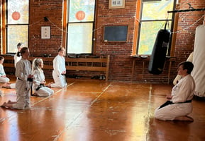 Several karate students, in gis, kneeling in meditation